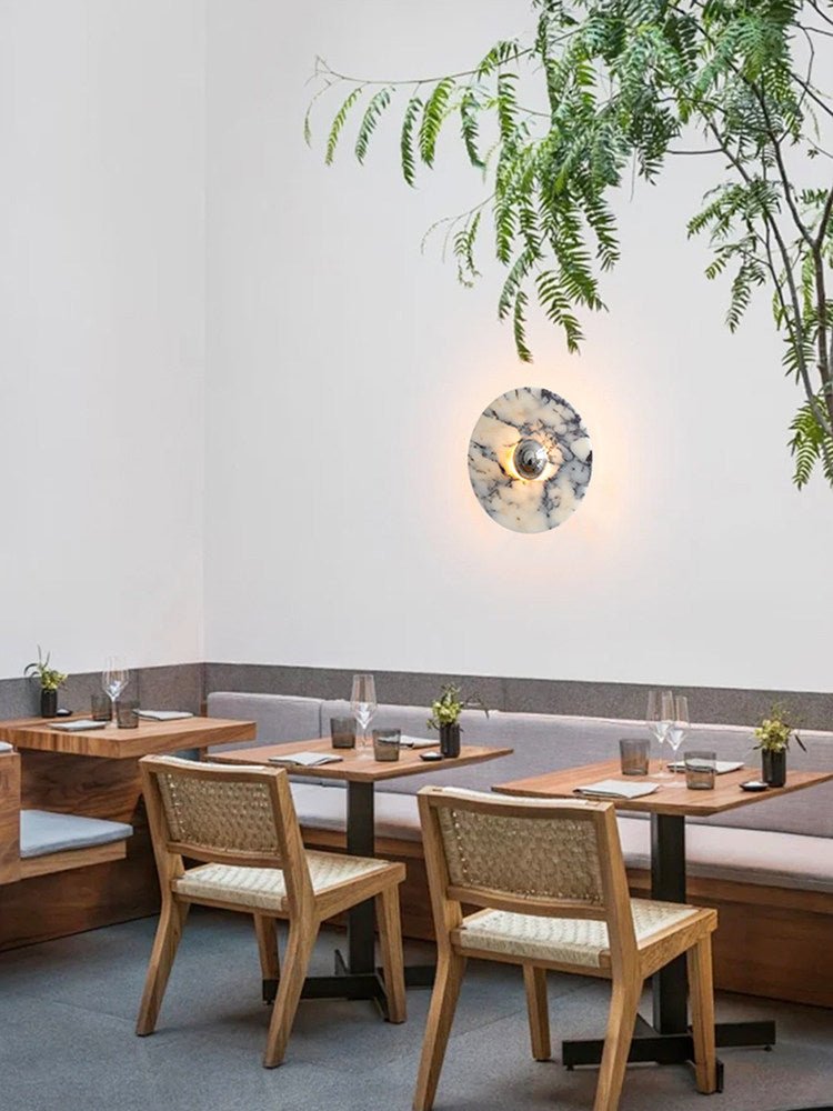 A wider dining-room crop of the glowing Clérachic wall light beside banquette seating and trailing greenery overhead.