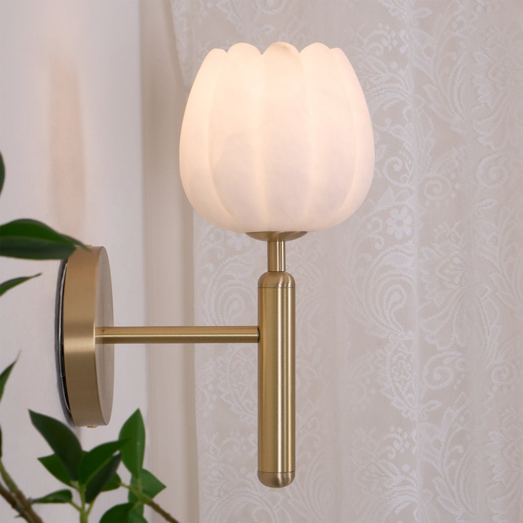 Close side view of the lit sconce against a lace curtain, showing the brass arm reaching out from the wall plate.