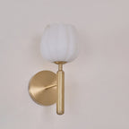 Brass sconce unlit on a pale pink-toned wall, the alabaster shade reading as plain matte white with the light off.