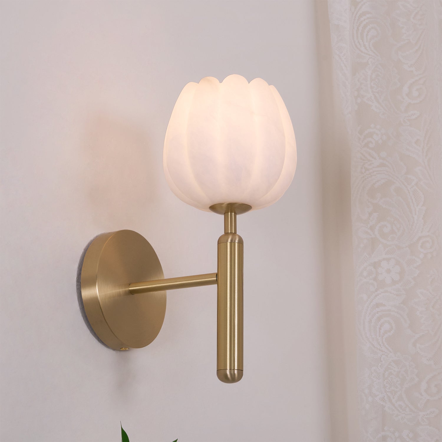 The brass Eurzorion wall light switched on beside a sheer curtain, shade glowing a soft warm white