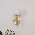 Eurzorion wall light seen head-on against a cream wall, with an olive sprig framing the lower corner