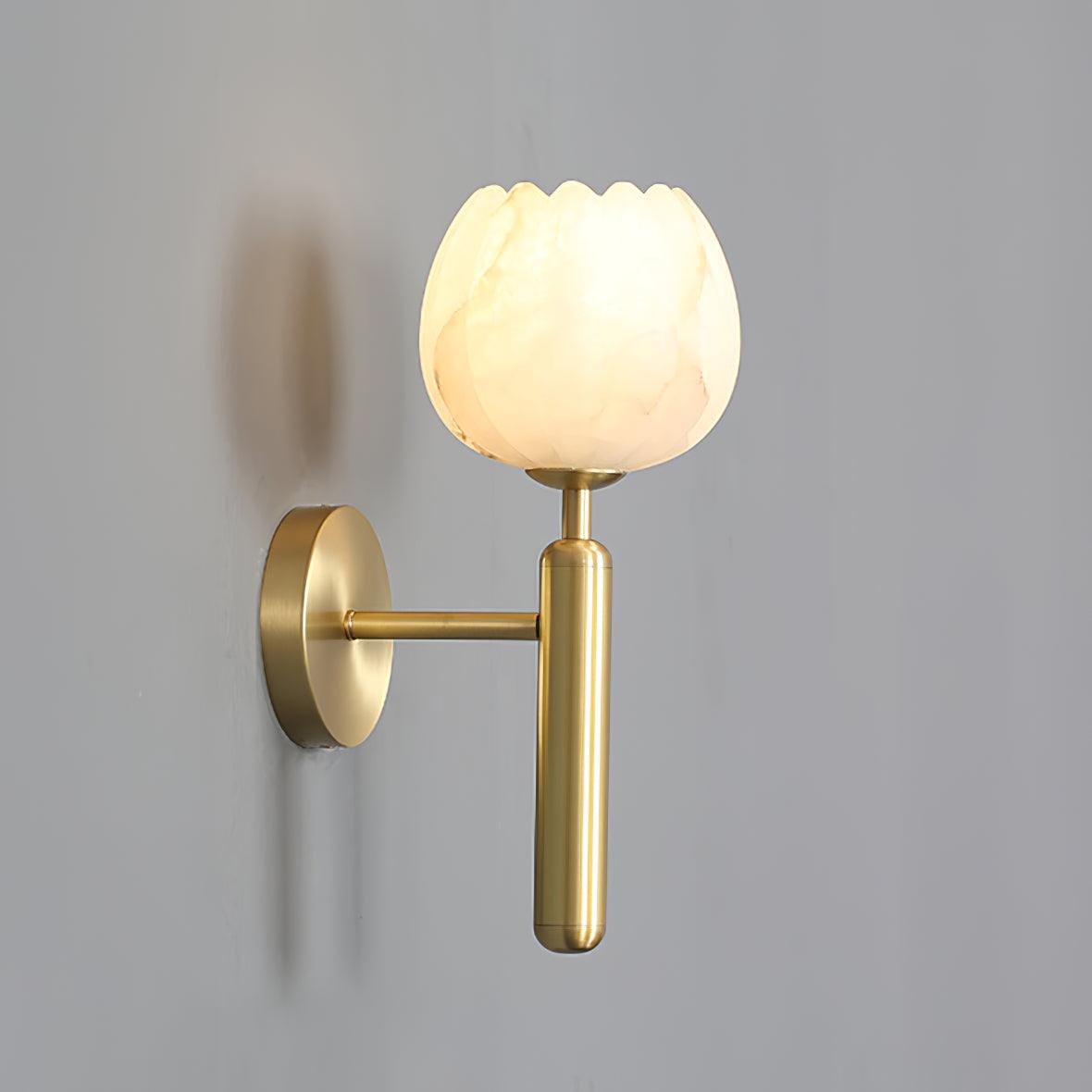 Angled side view of the lit brass sconce on a grey wall, the arm bracket and back plate clearly visible.