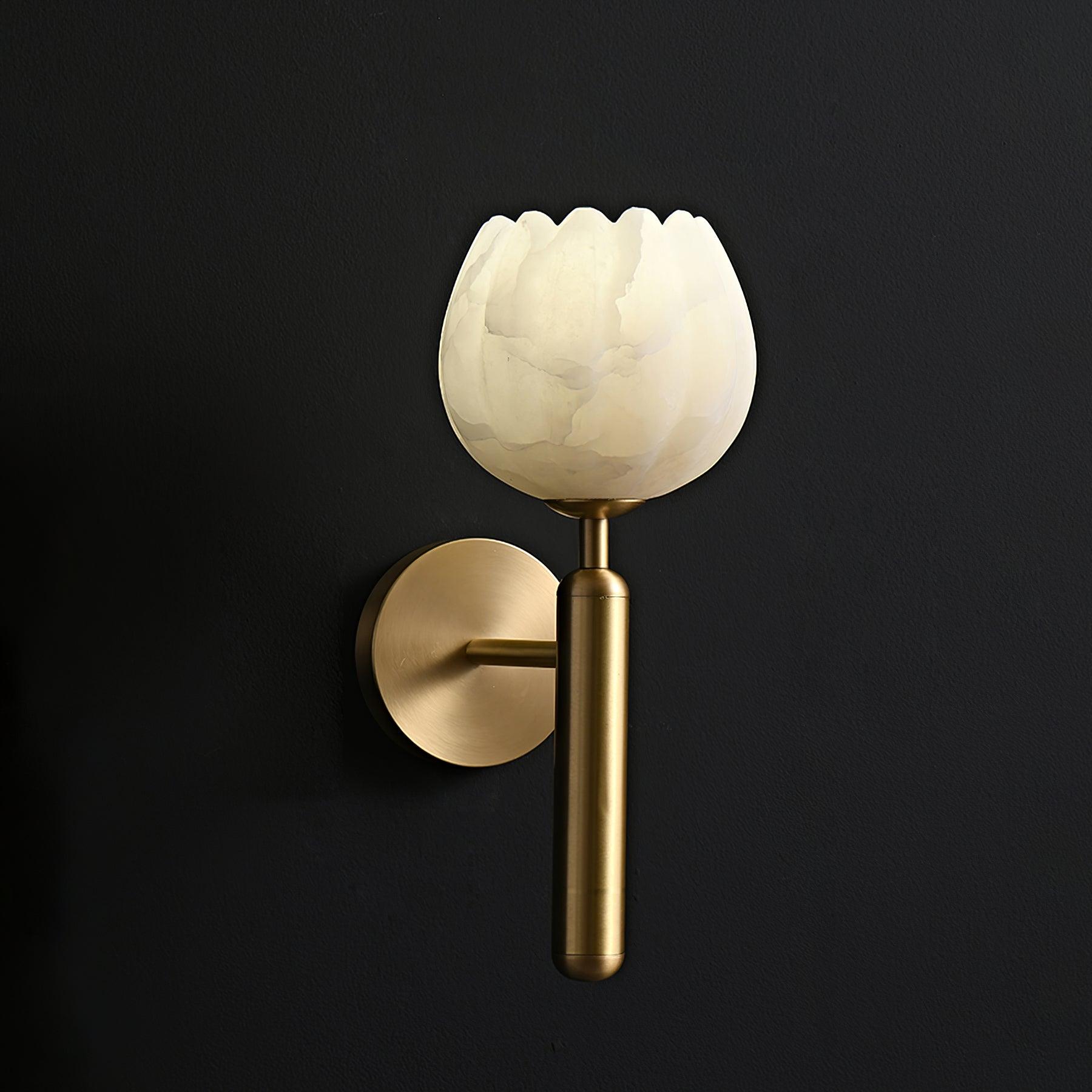 Angled view of the brass Eurzorion sconce on a black wall, the alabaster shade softly backlit
