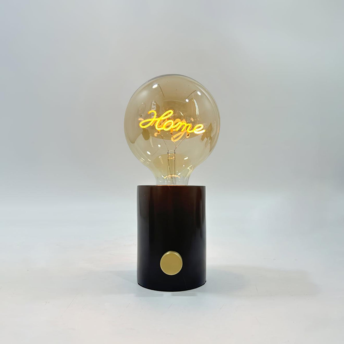 Close-up of the Clérachic novelty lamp's cognac-tinted bulb on its black marble base, the script filament glowing warmly.