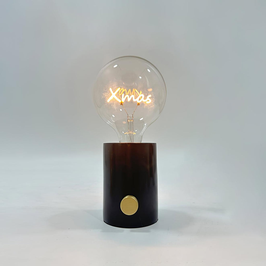 Close-up of the Clérachic novelty lamp's clear bulb on a dark marble base, its filament shaped like the word Xmas.