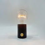 Close-up of the Clérachic novelty lamp's clear bulb on a dark marble base, its filament shaped like the word Xmas.