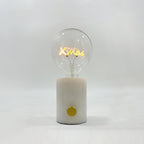 Close-up of the Clérachic novelty lamp's clear bulb on a white marble base, its filament shaped like the word Xmas.