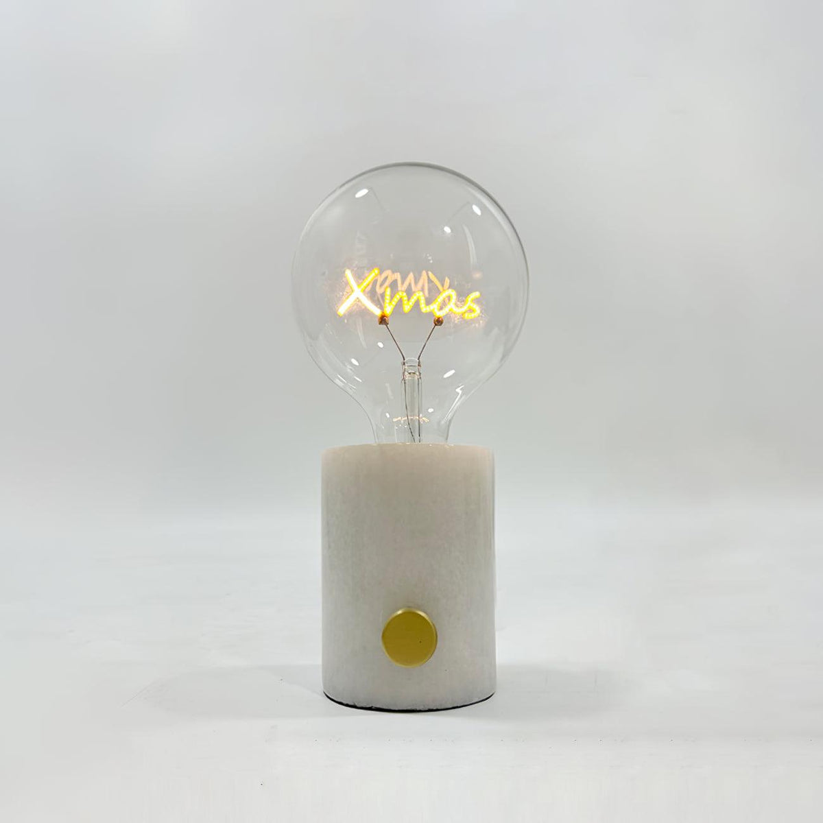 Close-up of the Clérachic novelty lamp's clear bulb on a white marble base, its filament shaped like the word Xmas.