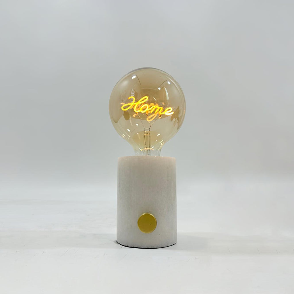The word Home glows in the filament of this Clérachic novelty lamp's cognac-tinted bulb, set on a white marble base.