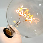 Macro close-up of the Clérachic novelty lamp's glass bulb, showing its script-shaped filament glowing inside.