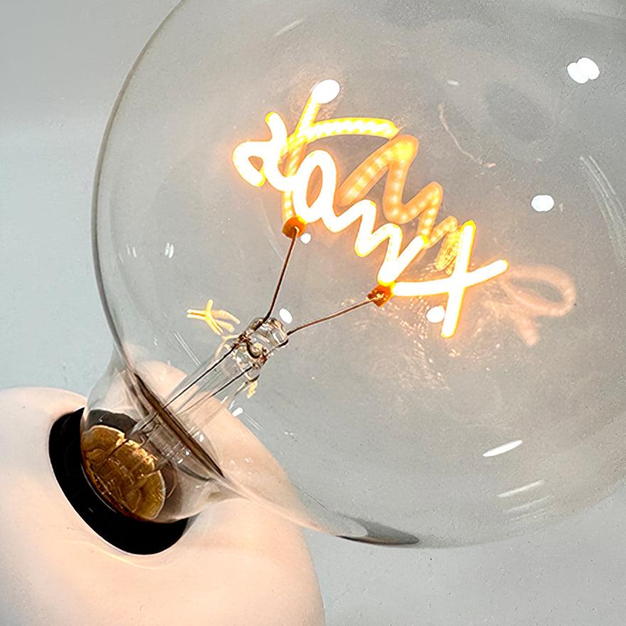 Macro close-up of the Clérachic novelty lamp's glass bulb, showing its script-shaped filament glowing inside.