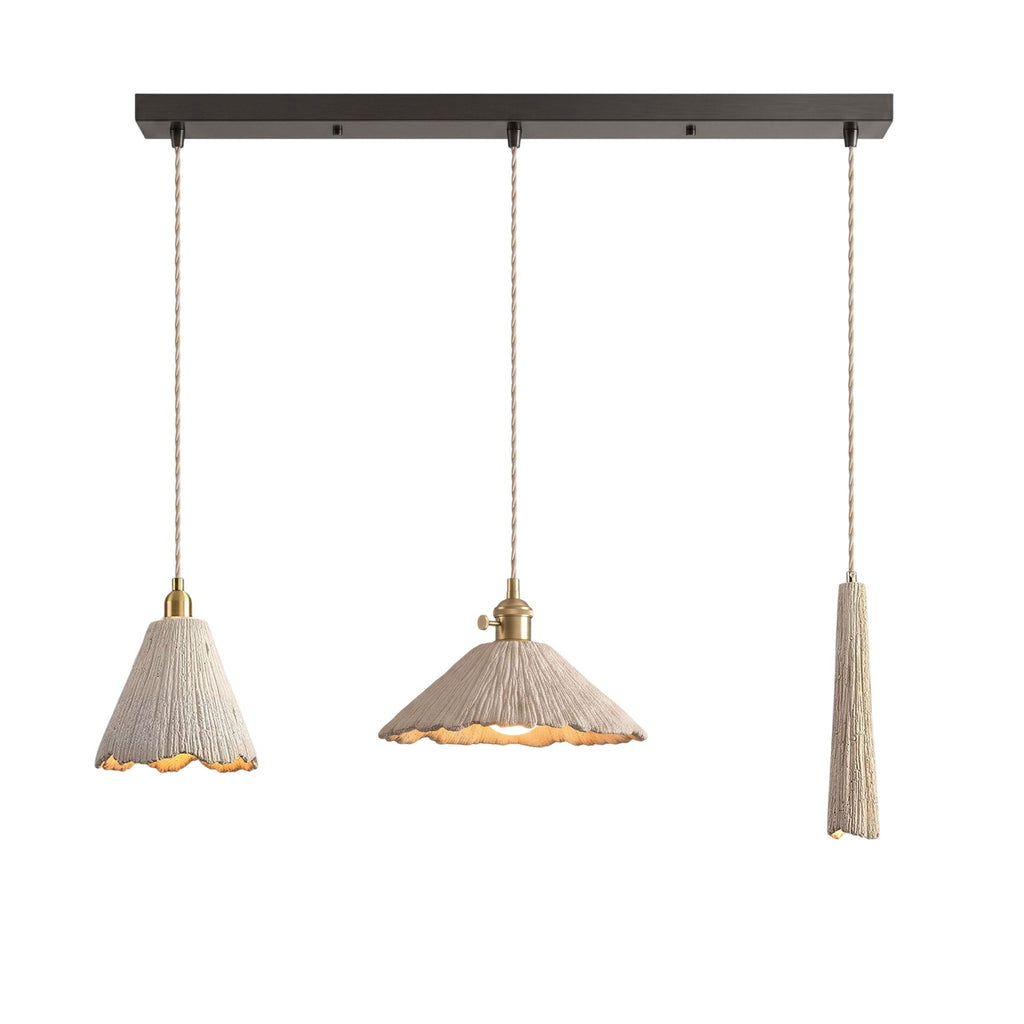 Three microcement pendants on a dark linear ceiling canopy: a tall scalloped cone, a wide scalloped cone and a slim tapered shade, each on a braided cord