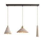 Three microcement pendants on a dark linear ceiling canopy: a tall scalloped cone, a wide scalloped cone and a slim tapered shade, each on a braided cord