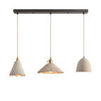 Three microcement pendants on a dark linear ceiling canopy: a tall scalloped cone, a wide scalloped cone and a small bell dome, each on a braided cord