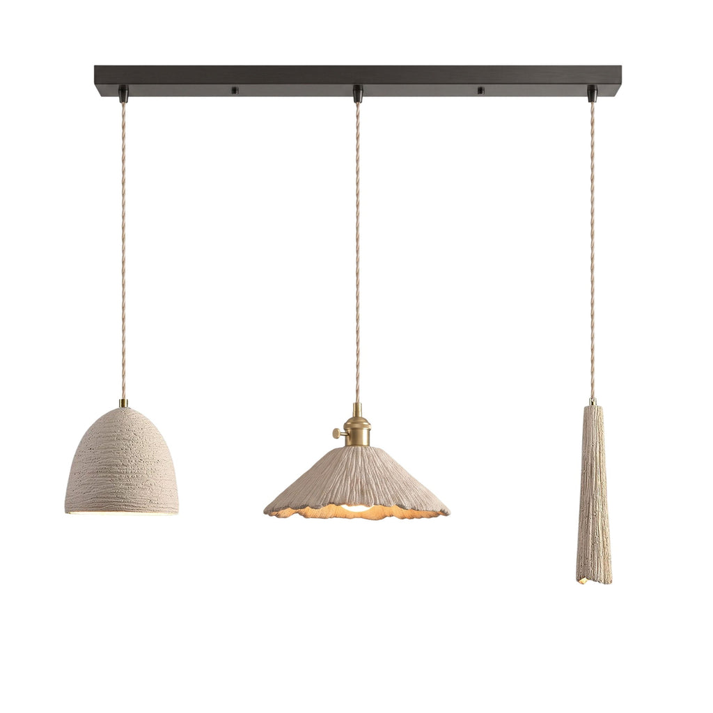 Three microcement pendants on a dark linear ceiling canopy: a small bell dome, a wide scalloped cone and a slim tapered shade, each on a braided cord