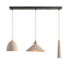 Three microcement pendants on a dark linear ceiling canopy: a small bell dome, a wide scalloped cone and a slim tapered shade, each on a braided cord