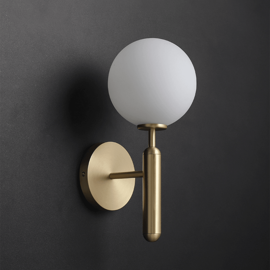 This brass Clérachic wall light with a white glass globe stands out against a near-black studio backdrop.