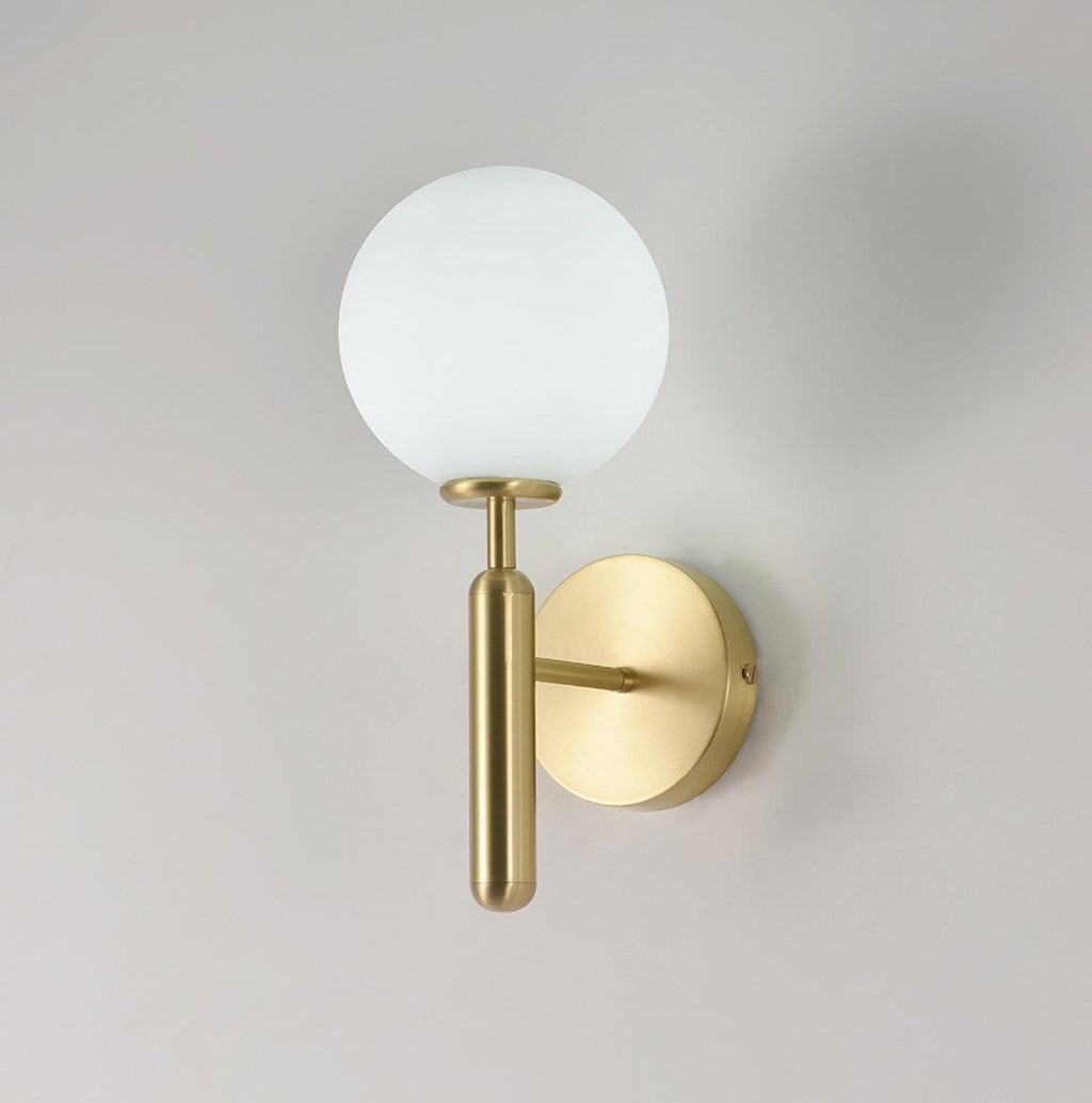 Unlit, this brass Clérachic wall light shows its round white glass globe against a plain light grey wall.