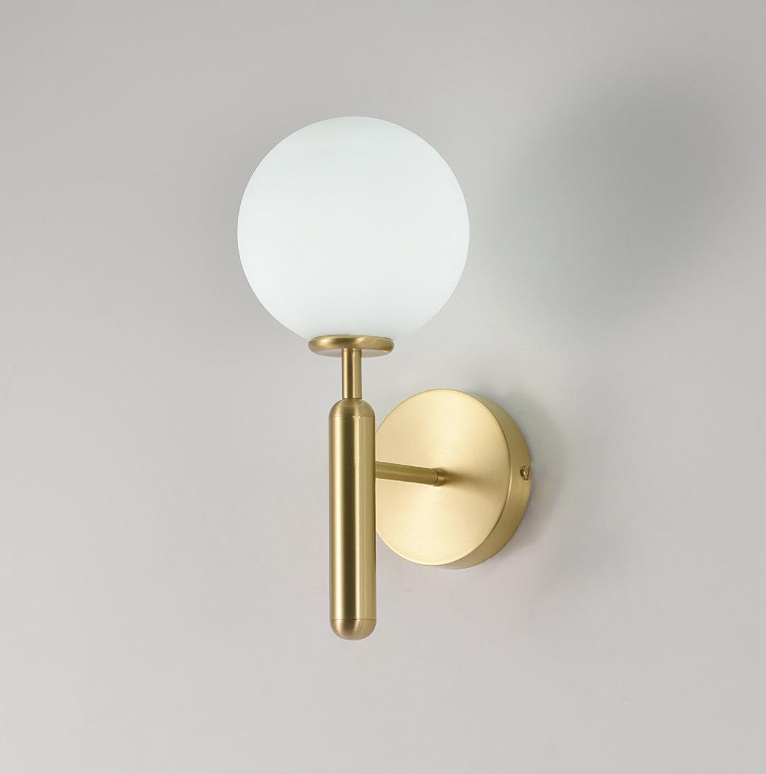 Unlit, this brass Clérachic wall light shows its round white glass globe against a plain light grey wall.