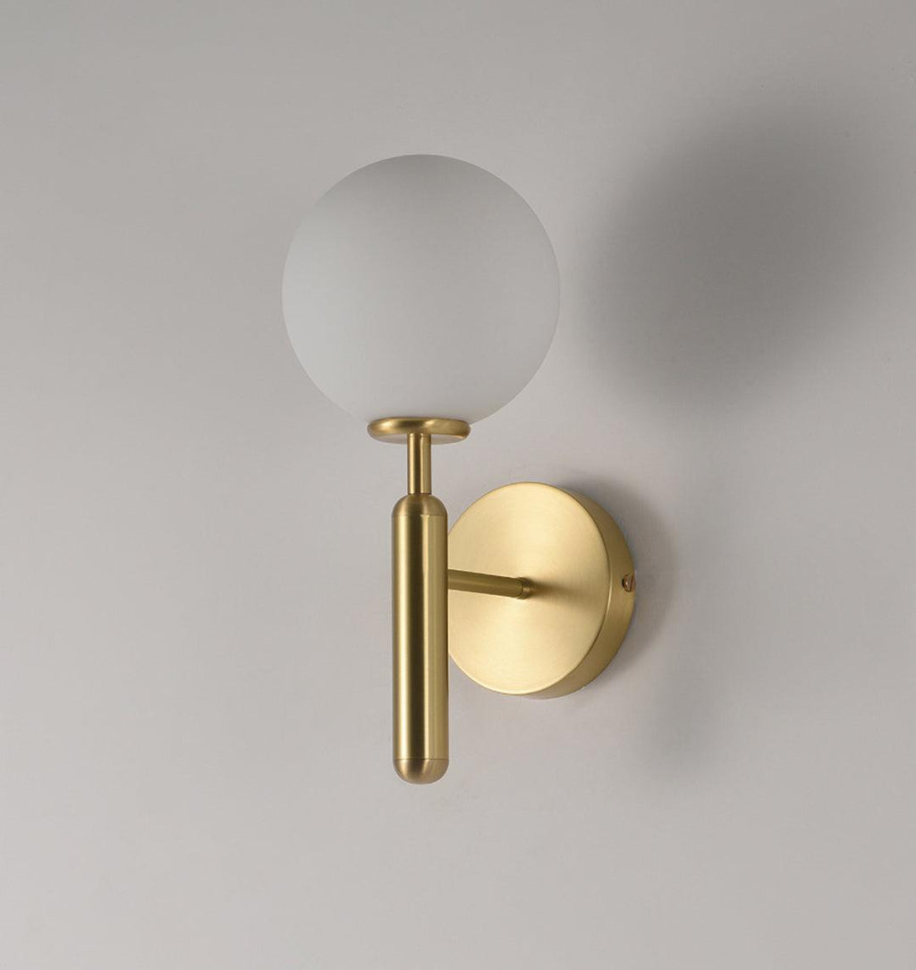 This brass Clérachic wall light with a frosted white glass globe casts a soft shadow on a light grey wall.