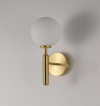 This brass Clérachic wall light with a frosted white glass globe casts a soft shadow on a light grey wall.