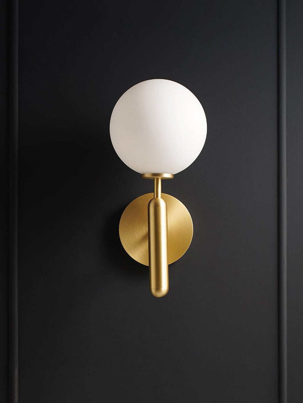 Lit against a near-black door, this brass Clérachic wall light's round white glass globe stands out clearly.