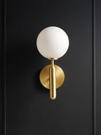 Lit against a near-black door, this brass Clérachic wall light's round white glass globe stands out clearly.