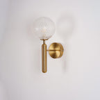 Softly shadowed, this brass Clérachic wall light's dimpled clear glass globe sits against a plain white wall.