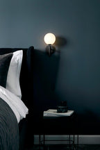 In a deep teal bedroom, this black Clérachic wall light glows above a nightstand with books and a candle.