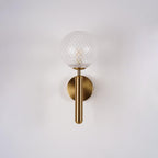 This brass Clérachic wall light shows its dimpled clear glass globe and slender arm against a plain white wall.