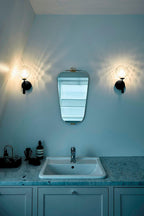Either side of a mirror, two black Clérachic wall lights with dimpled clear glass globes light a teal bathroom with a marble vanity.
