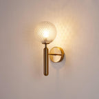 Warmly lit, this brass Clérachic wall light's dimpled clear glass globe glows against a plain cream wall.