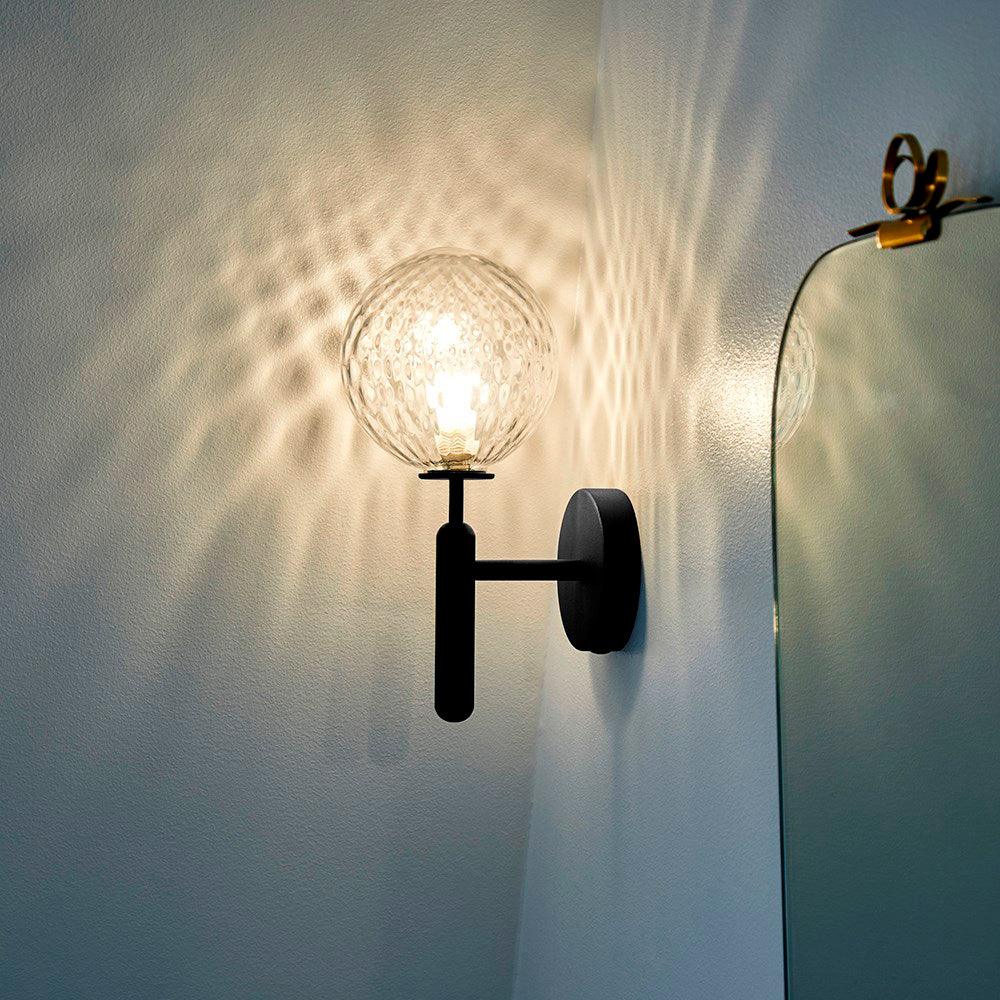 Beside an ornate mirror, this black Clérachic wall light's dimpled clear glass globe casts light across a blue wall.