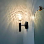 Beside an ornate mirror, this black Clérachic wall light's dimpled clear glass globe casts light across a blue wall.