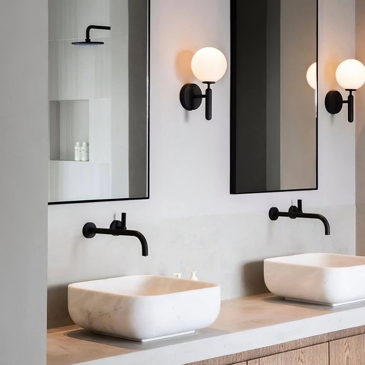 Between two mirrors above a marble vessel sink with a black tap, this black Clérachic wall light glows in a bathroom.