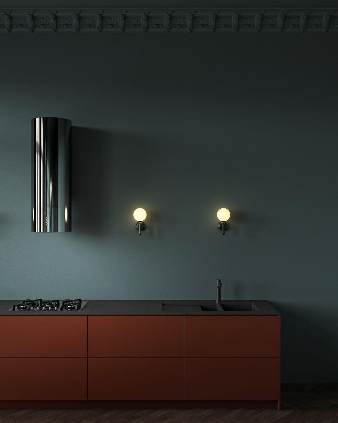 In a kitchen with rust-coloured cabinetry, two black Clérachic wall lights glow beside a chrome extractor hood.