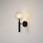 A close view shows this black Clérachic wall light's dimpled clear glass globe casting a honeycomb pattern on the wall.