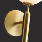 Close view of the brushed brass mounting plate and arm on this Clérachic wall light, with its white glass globe just visible above.