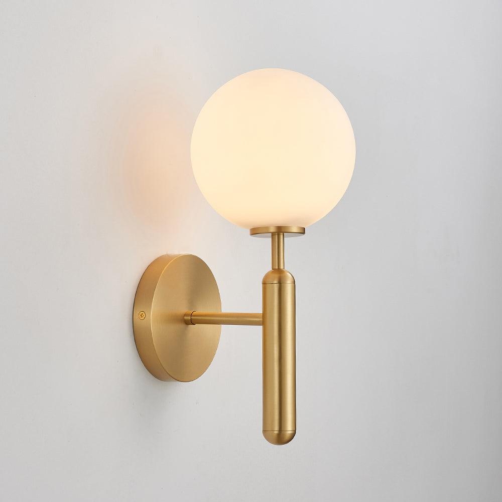 Unlit, this brass Clérachic wall light shows its round white glass globe against a plain grey wall.