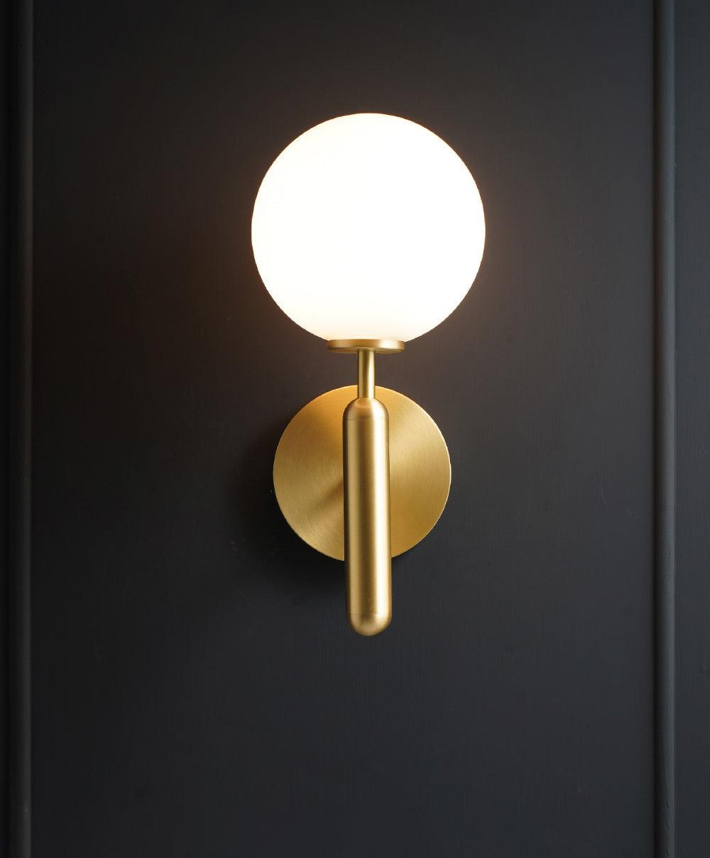 Set against a dark charcoal panelled wall, this brass Clérachic wall light's white glass globe glows softly.