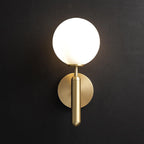 This brass Clérachic wall light with a lit white glass globe stands out against a near-black wall.