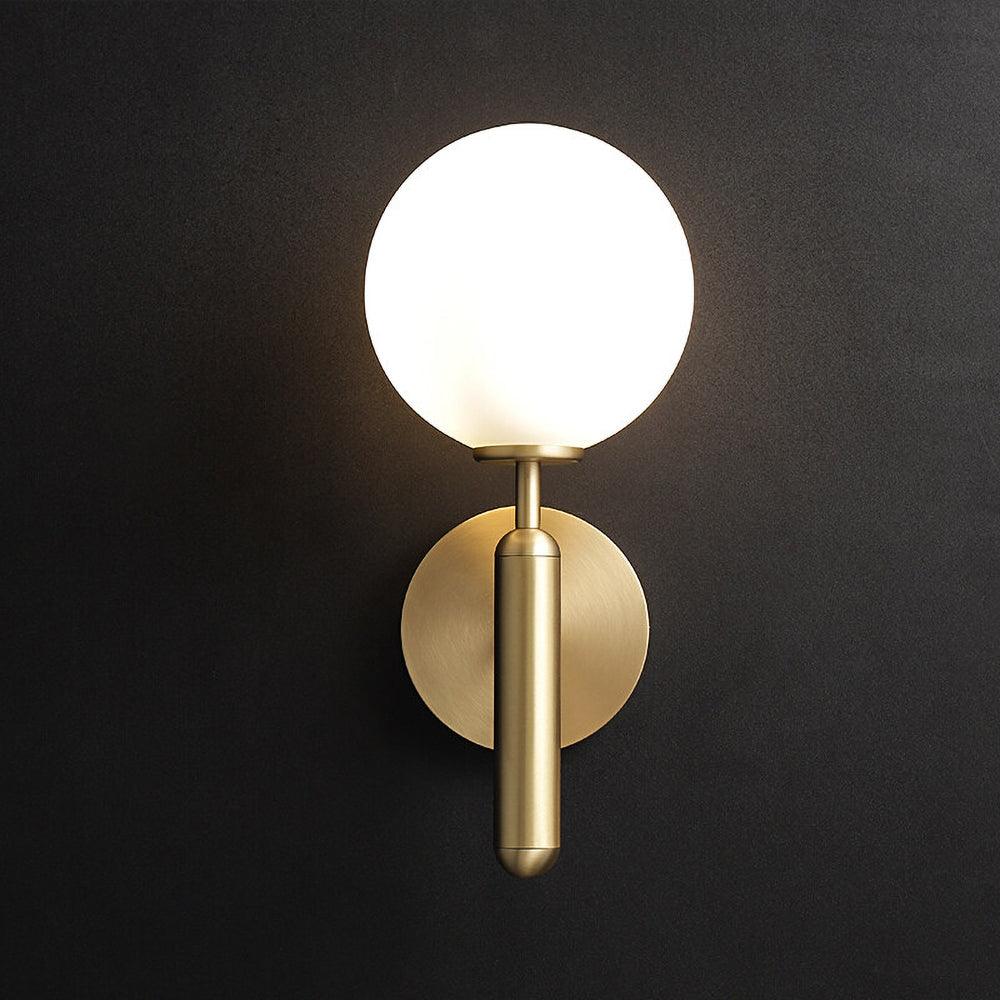 This brass Clérachic wall light with a lit white glass globe stands out against a near-black wall.