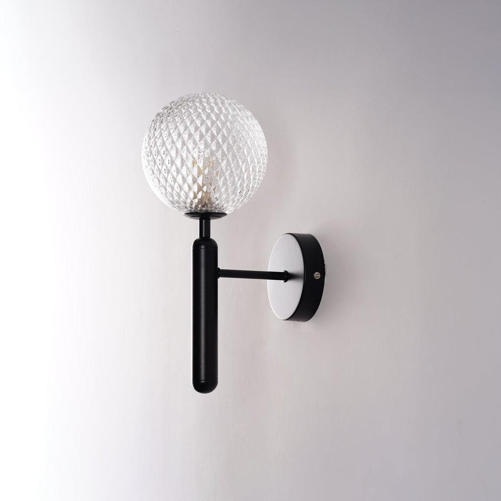 Unlit, this black Clérachic wall light shows its dimpled clear glass globe at an angle against a light grey wall.