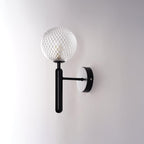 Unlit, this black Clérachic wall light shows its dimpled clear glass globe at an angle against a light grey wall.