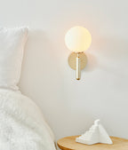This Clérachic wall light in brushed brass glows above a bedside table with a folded pillow and a small white sculpture.