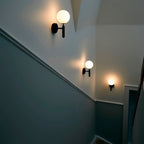 Three black Clérachic wall lights with glowing white globes trace a stairwell wall painted deep teal.