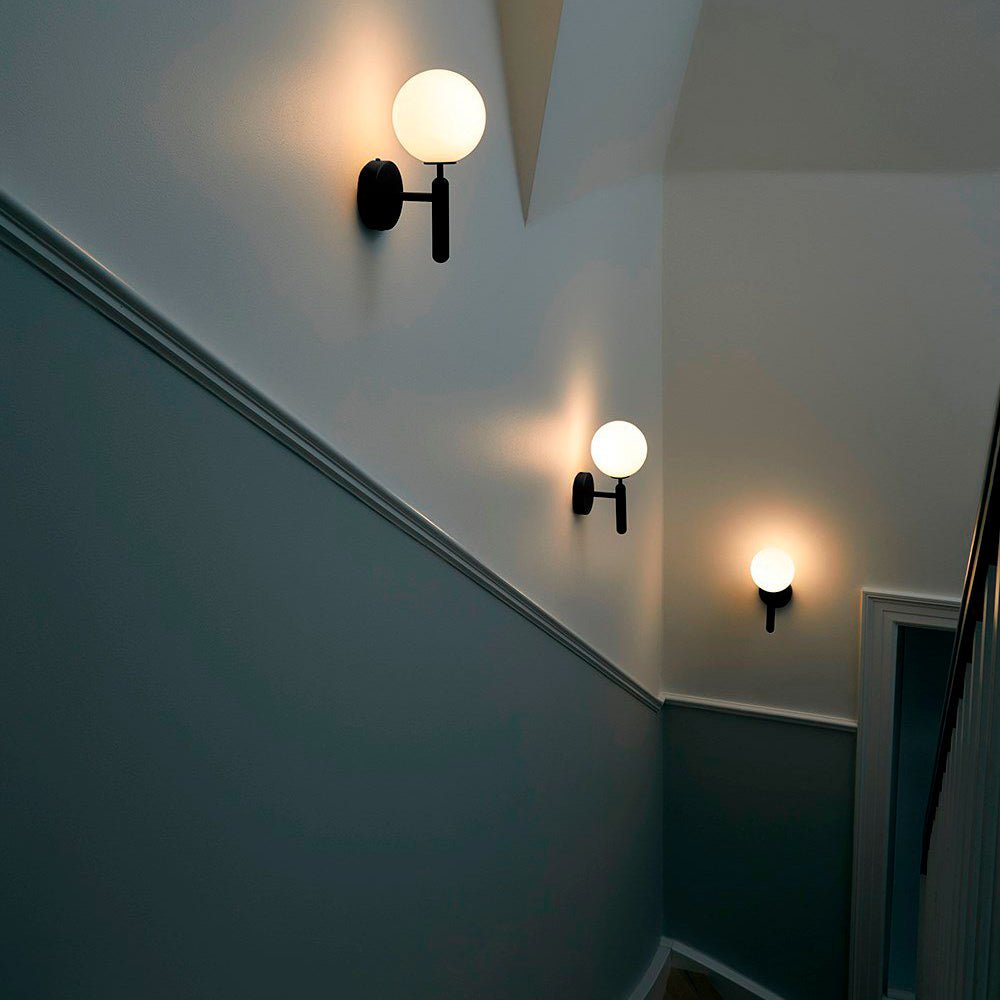 Three black Clérachic wall lights with glowing white globes trace a stairwell wall painted deep teal.