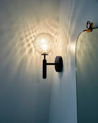 Close to an ornate mirror, this black Clérachic wall light casts light through its dimpled clear glass globe onto the wall behind.
