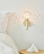 With a dimpled clear glass globe casting a honeycomb pattern of light, this brass Clérachic wall light sits above a bedside table.