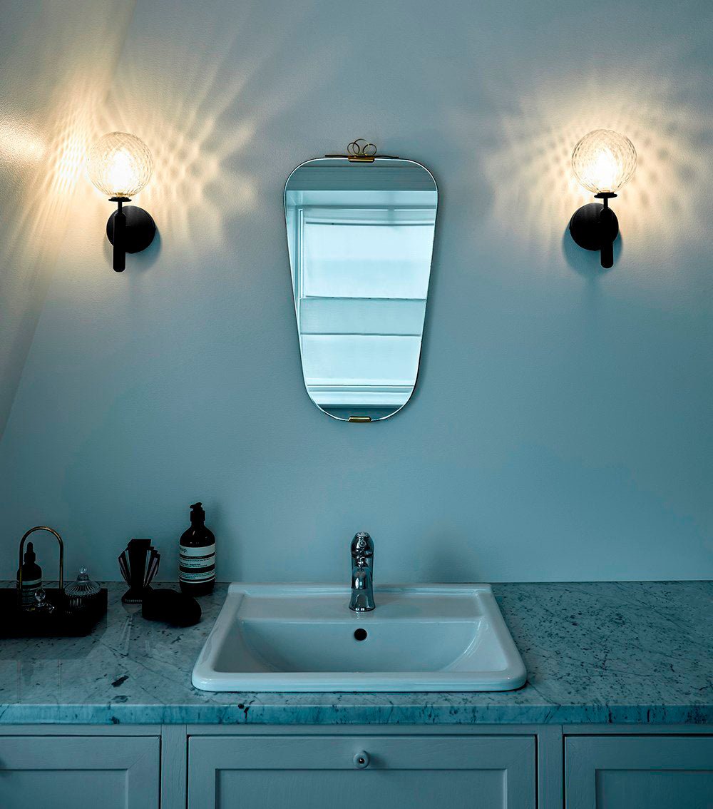 Flanking a tall arched mirror, two black Clérachic wall lights with dimpled clear glass globes glow above a teal-marble vanity.